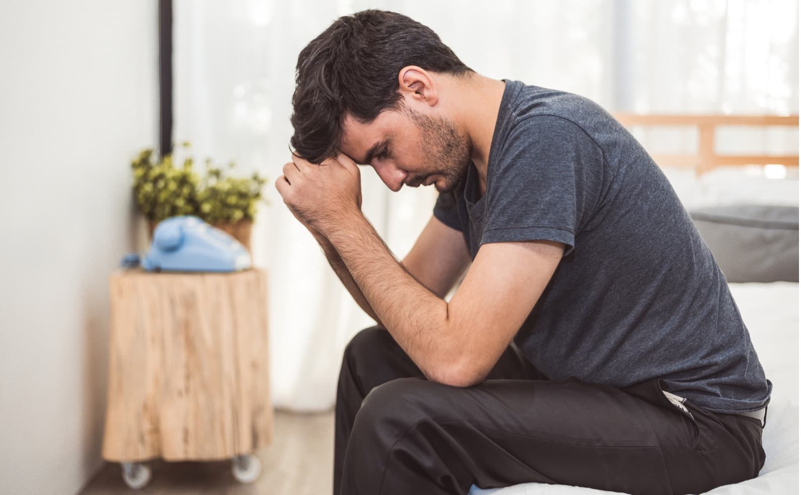 Man sitting on the edge of a bed with his head in his hands